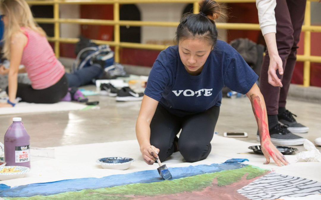 Student paints UChicago Homecoming banner in Crown Fieldhouse wearing a shirt that reads "vote"