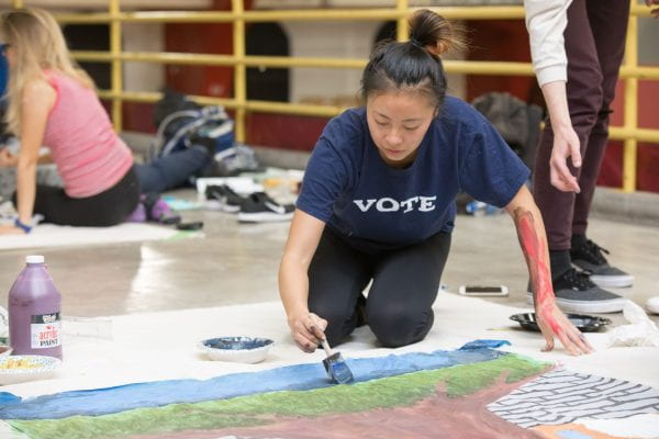 Student paints UChicago Homecoming banner in Crown Fieldhouse wearing a shirt that reads "vote"